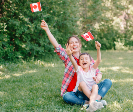 A white woman and child sitting on a green lawn. Both are waving Canada flags.